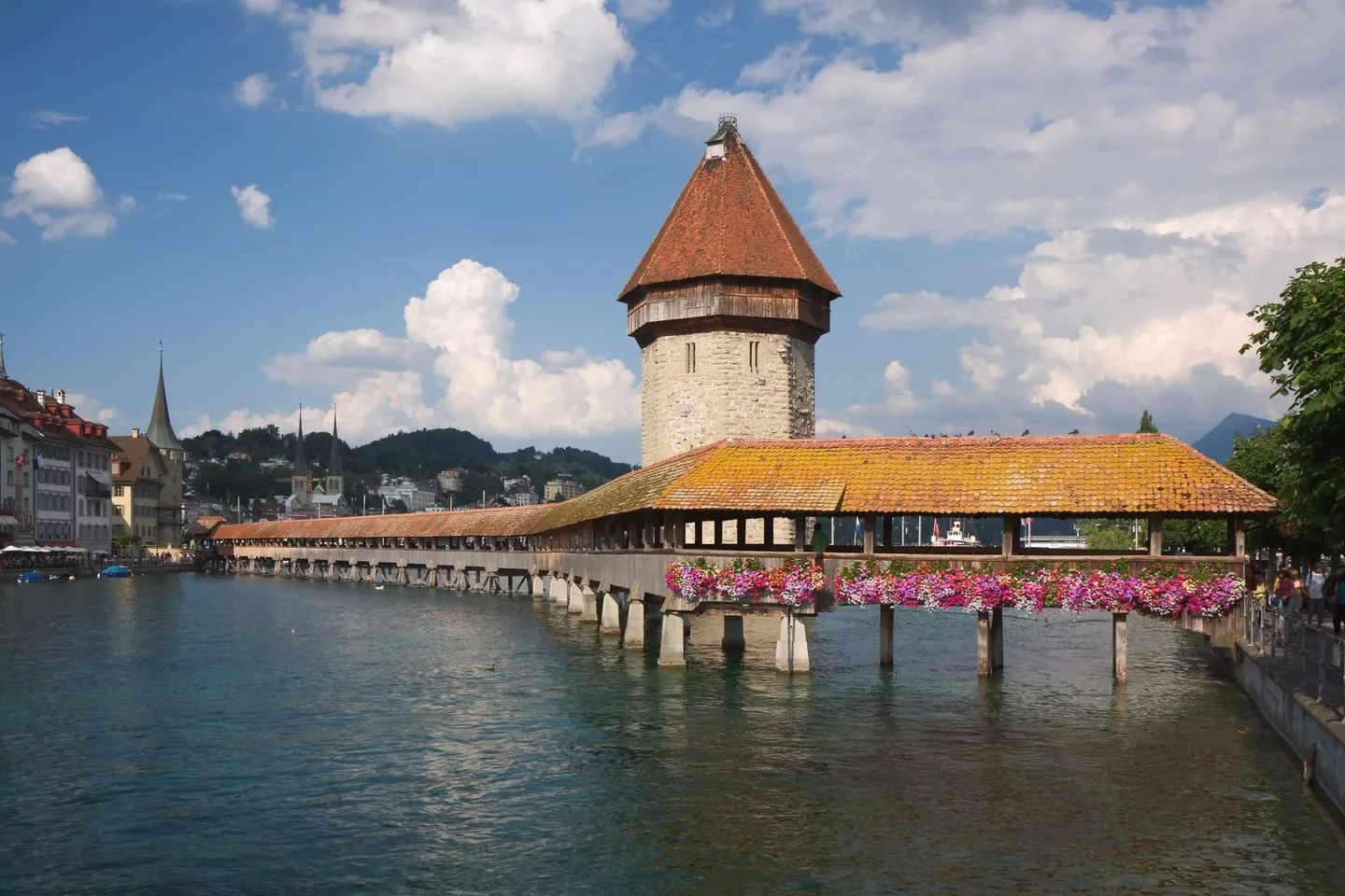 The covered wooden Chapel Bridge with flower boxes and its octagonal stone water tower on the River Reuss in Lucerne