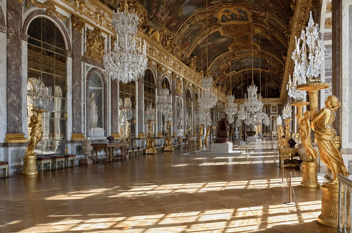 The Hall of Mirrors at Versailles, lined with chandeliers, gilded statues and arched mirrors