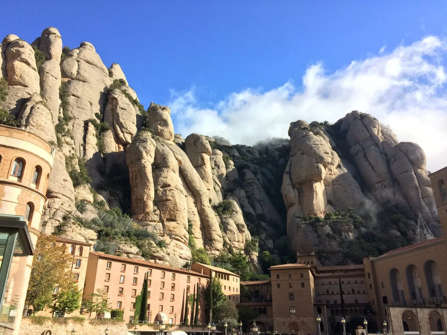 Montserrat monastery buildings at the foot of rounded, sheer rock pinnacles under a blue sky