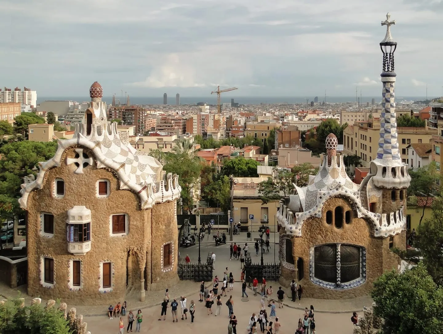 The two mosaic-roofed gatehouse pavilions at the entrance of Park Güell, with the city stretching to the sea behind them