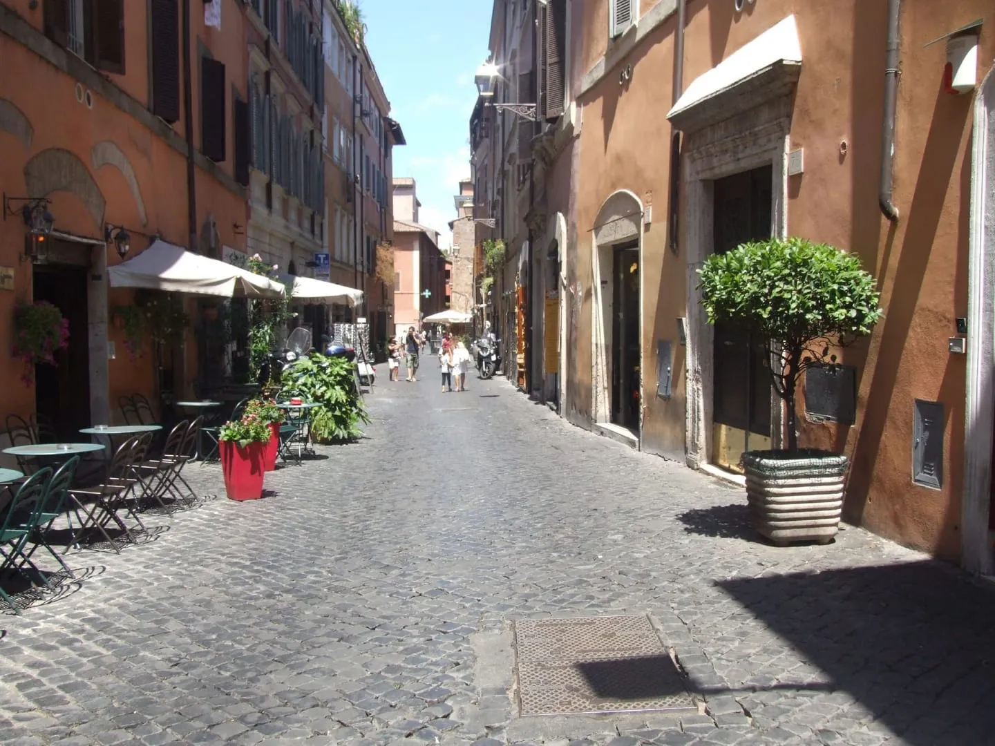 A quiet cobbled street in Trastevere lined with orange buildings, cafe tables and potted plants